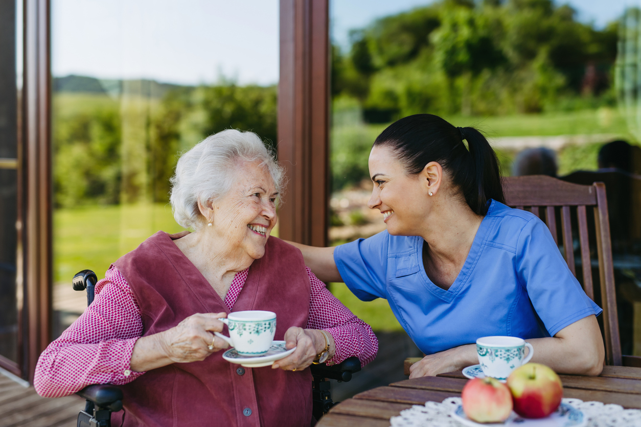 A caregiver sharing tea with a smiling older woman outdoors
